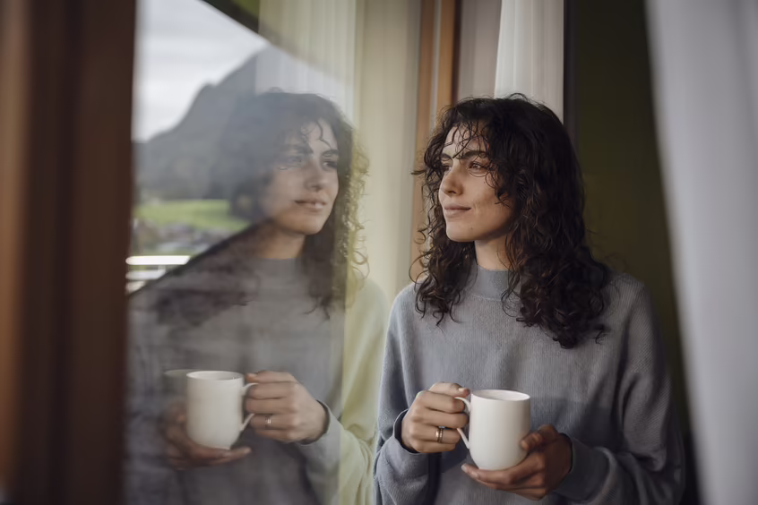 DAS SIEBEN - sieben Sinne - sehen - Morgenmoment mit Weitblick ©alexgretter Frau mit Tasse auf einem Balkon mit Blick auf Berge und Landschaft im DAS SIEBEN