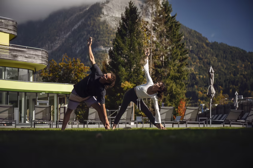 DAS SIEBEN - Yoga im Freien ©alexgretter Zwei Personen machen Yoga auf einer Wiese vor dem Hotel DAS SIEBEN