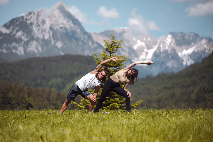 DAS SIEBEN - Yoga im Freien ©alexgretter Zwei Personen machen Yoga auf einer Wiese vor dem Hotel DAS SIEBEN